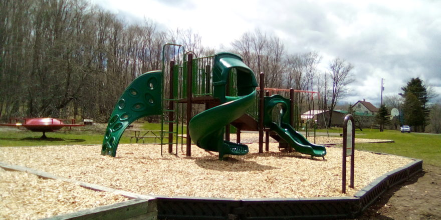 Playground Equipment completed spring of 2020. Green and brown slides and climbing platforms and ladders surrounded by woodchips and free form black borders.