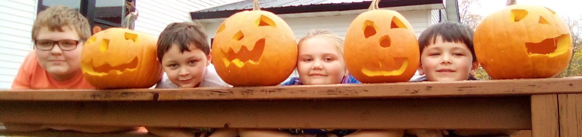 Reggie,Oliver,Olivia,and Justin holding their carved pumpkins on the railing of the school.