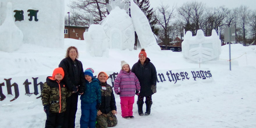 Justin, Ms. J., Oliver, Reggie, Olivia, and Ms. Christine stand in front of one of the large snow sculptures at MTU 2022.
