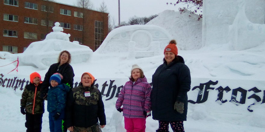 Justin, Ms. J., Oliver,, Reggie, Olivia, and Ms. Christine stand in front of a snow sculpture at MTU 2022.
