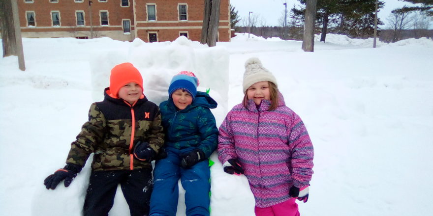 Justin, Oliver, and Olivia sitting on a snow sculpture at MTU.
