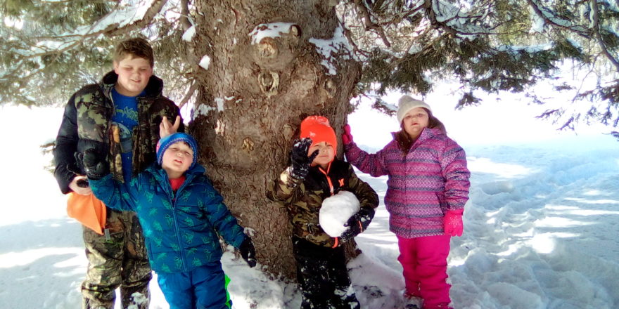 Reggie, Oliver, Justin, and Olivia rest under a tree during snowshoeing at Omer's Golf Course.