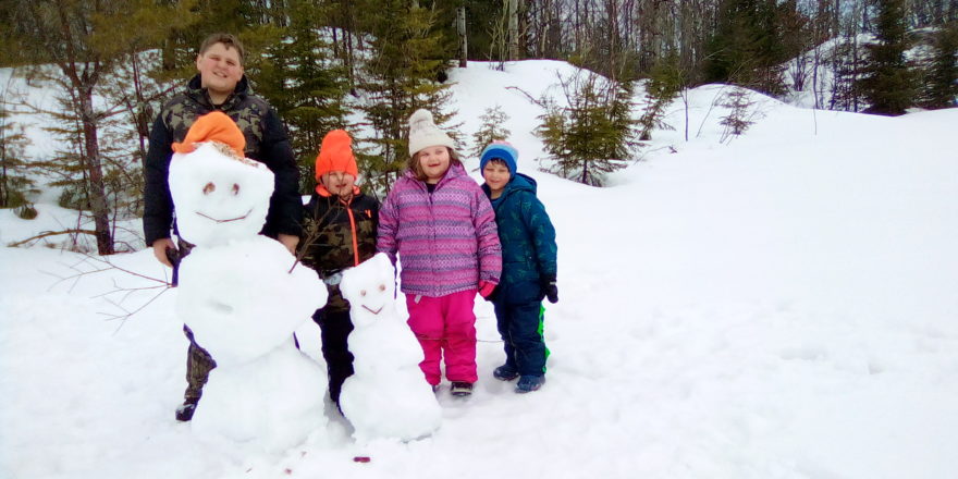 Reggie Justin, Olivia, and Oliver standing behind the snow kids they made at the school pond.