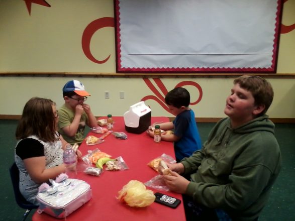 Olivia, Justin, Oliver, and Reggie eating lunch in the break room at the Children's Museum.
