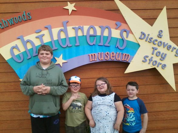 Reggie, Justin, Olivia, and Oliver standing under the sign at the Children's Museum.