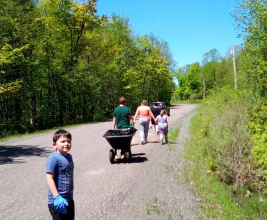 Picking up trash on Winona Rd with Justin bringing up the rear, then Reggie pulling the wheel barrow and Ms. J walking with Oliver, and Ms. Christine up front along with Olivia.