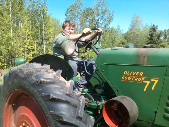 Reggie sitting on the green and yellow Oliver row crop 77 tractor at Melody acre stables.