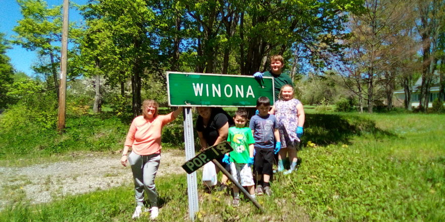 Ms. J. Ms. Christine, Oliver, Justin, Olivia, and Reggie standing around the Winona sign after cleaning up the road of trash for earth day.