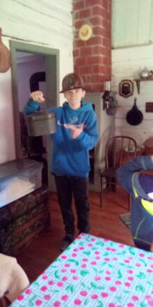 Jacob wearing a copper mine carbide lit helmet and holding his metal lunch container..