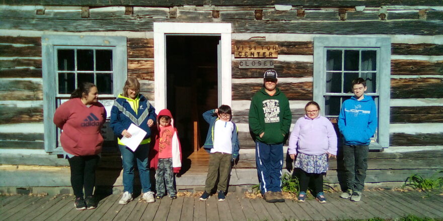 Ms. Christine, Ms. J., Oliver,, Justin, Reggie, Olivia, and Jacob standing outside the entrance of Old Victoria visitor center.