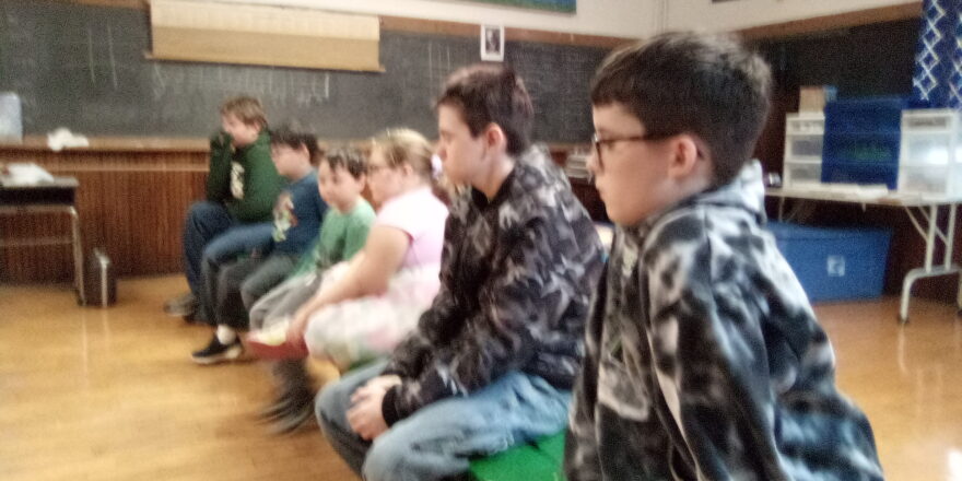 Reggie, Justin, Oliver, Olivia, Jacob, and Avery sitting on the bench in class listening to fire fighters.