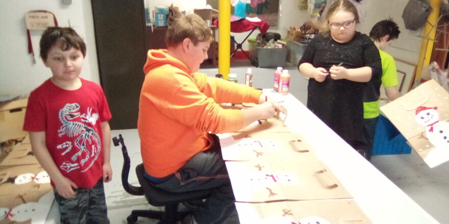 Oliver, Reggie, and Olivia painting snowman decor on the bags for Little Brothers.