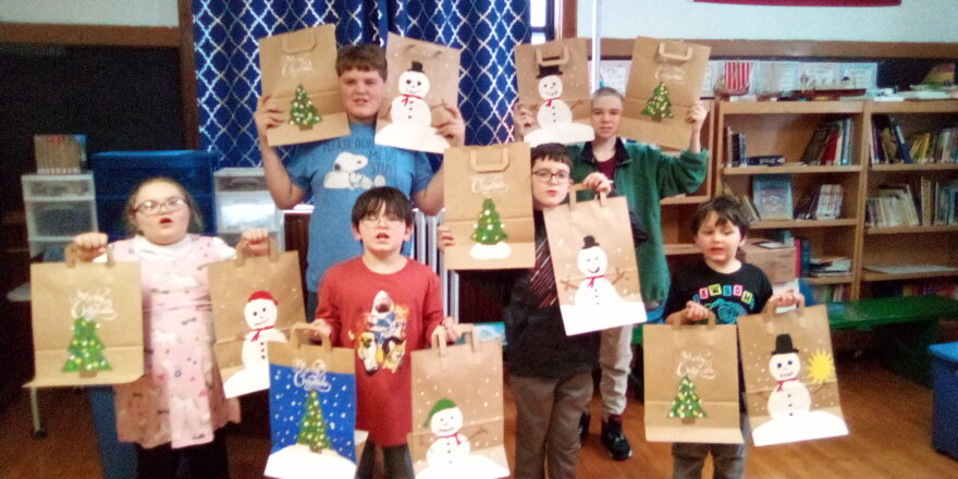 Christmas 2022 kids holding the snowman and Christmas tree bags they decorated for Little Friends of the Elderly.