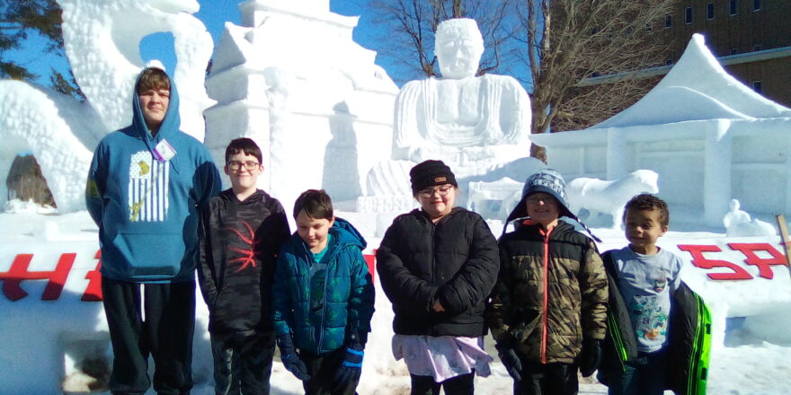 Kids standing in front of a snow sculpture at MTU.