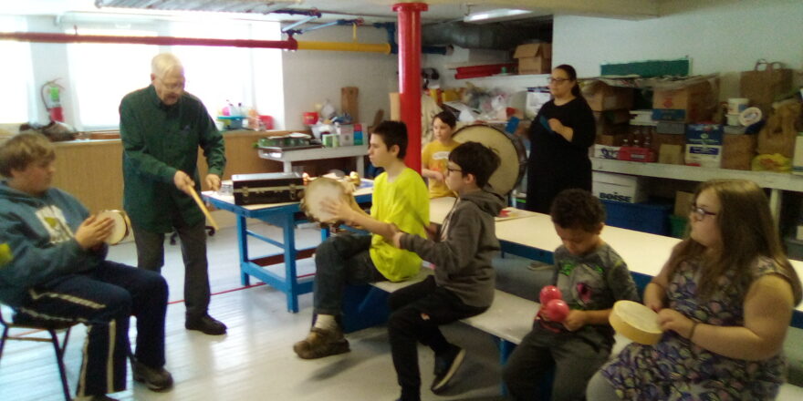 Music lesson with all the kids. Each student is holding a different percussion instrument and learning how to keep time.