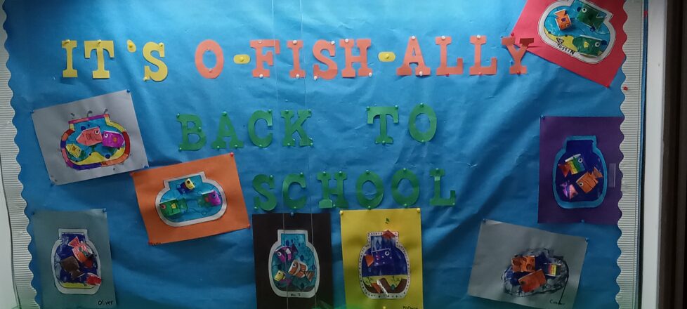 Back to school bulletin board "It's O-FISH-ALLY Back To School!" in bold colors and art pictures of fish bowls with fish swimming around in them from each student.
