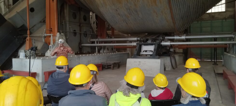 Students listening to the tour guide explain the big hoist drum that the cable was wrapped around to pull up the copper and miners.