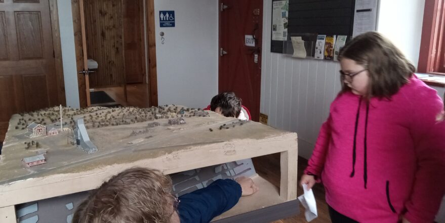 Student and teacher looking at model of mine site above ground and underground where shafts and stope levels are.