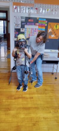 Fire Department in the class room putting on the air respirator on one of the students.