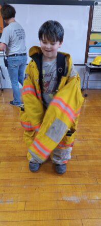 One of the 3rd grade students trying on a fire fighter's jacket and pants.