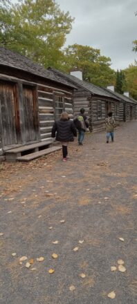 Students were walking around the living quarters of the log cabins just outside the fort gates. 