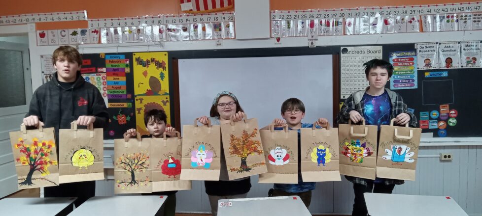 Our school kids holding up bags decorated for Little Brothers Friends of the Elderly. Trees with different colored fall leaves painted, Turkeys that are disguised as other characters like minions, deck of cards, and an owl.