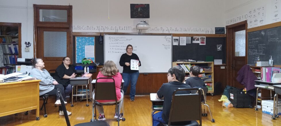 Ms. Kathy telling the kids about nutrition and hygiene in the front of the room while holding a poster of examples.