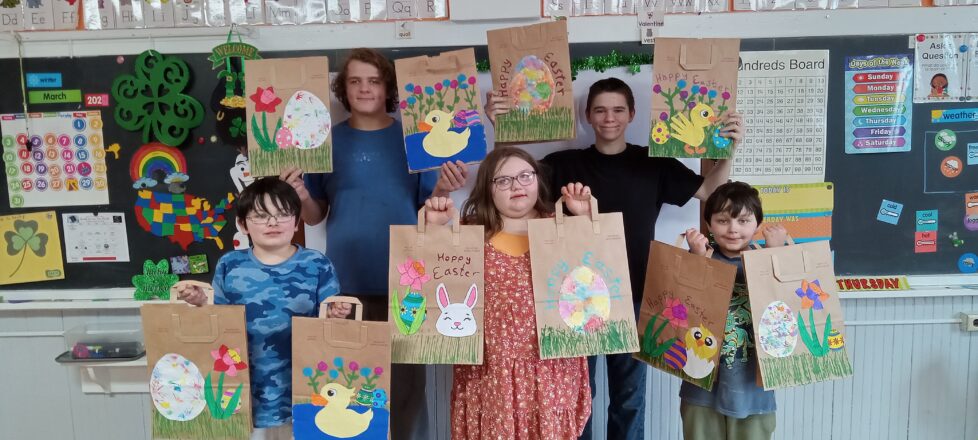 The kids are holding up the Easter bags they decorated before Friends of the Elderly come to pick them up. All 5 kids were holding differently decorated bags in each hand.